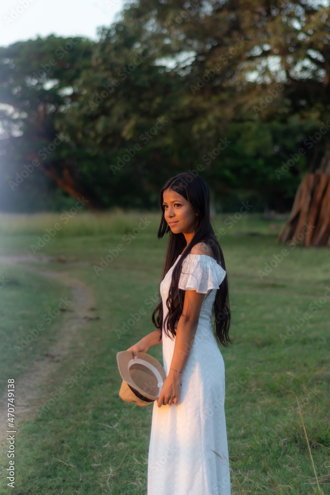 Naklejka premium Black hair brunette woman standing in the field outdoors. Caucasian brunette teen in white dress walking in the countryside 
