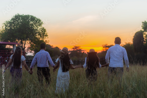 back view of united family  parents and children holding hands walking through the field at sunset 