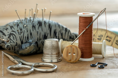 Close up of sewing kit consisting of thimble, needle, button, spools of thread, clasp, scissors, pad with pins and measuring tape.