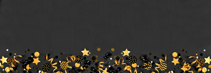 New Years party bottom border with glittery black and gold streamers and confetti. Top down view on a black background.