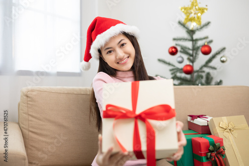 Beautiful Asian woman showing present gift box into camera. Young Happy cute girl celebrate in christmas holiday festival giving gift box sitting on sofa at home