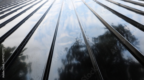 Metal sheet wall with reflection. The modern warehouse wall is made of black metal panels and has the reflection of the trees and sky in the bottom view. selective focus