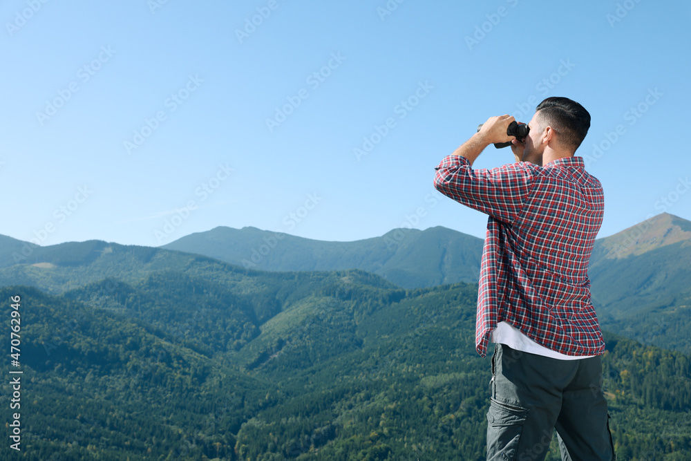 Man looking through binoculars in mountains on sunny day