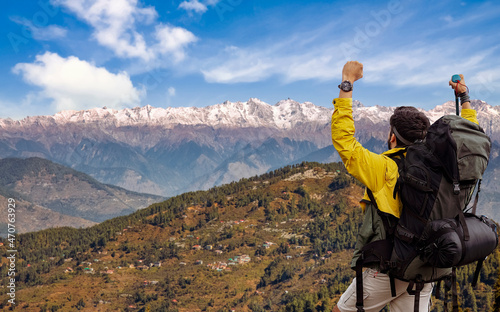 Male tourist hiker exults with raised arms on trek at Sangla, Himachal Pradesh, India with scenic Himalaya mountain landscape