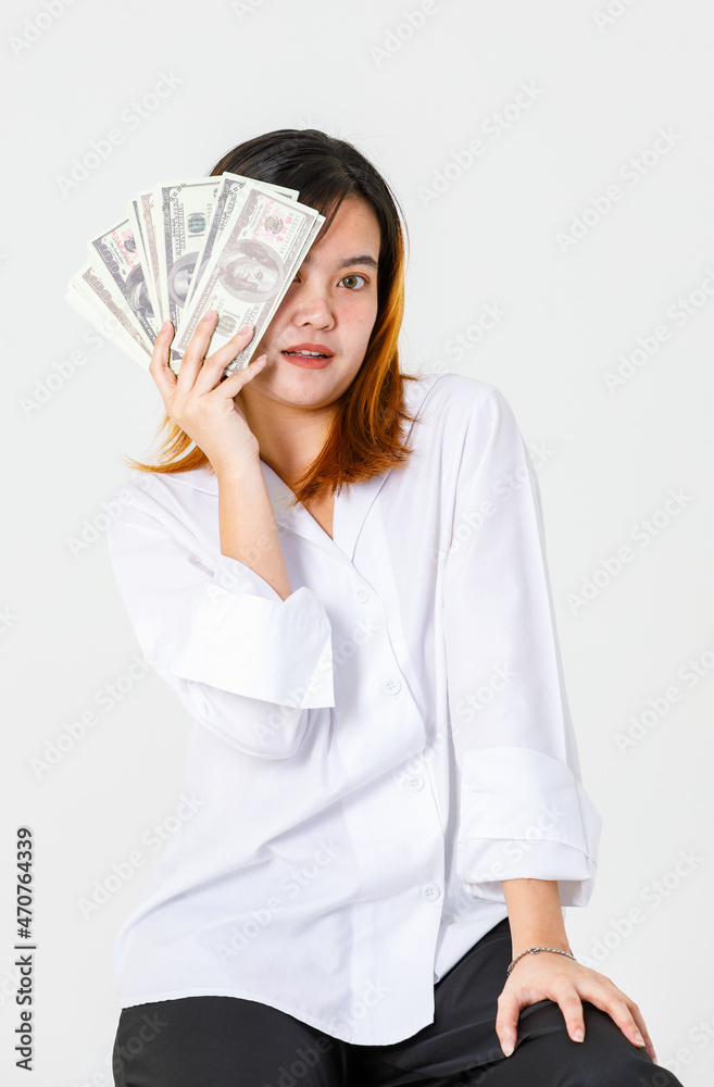 Portrait studio shot of Asian rich wealth female businesswoman model in casual wears sitting look at camera holding hundred dollars USD cash banknote currency stack cover face on white background Portrait studio shot of Asian rich wealth female businesswoman model in casual wears sitting look at camera holding hundred dollars USD cash banknote currency stack cover face on white background