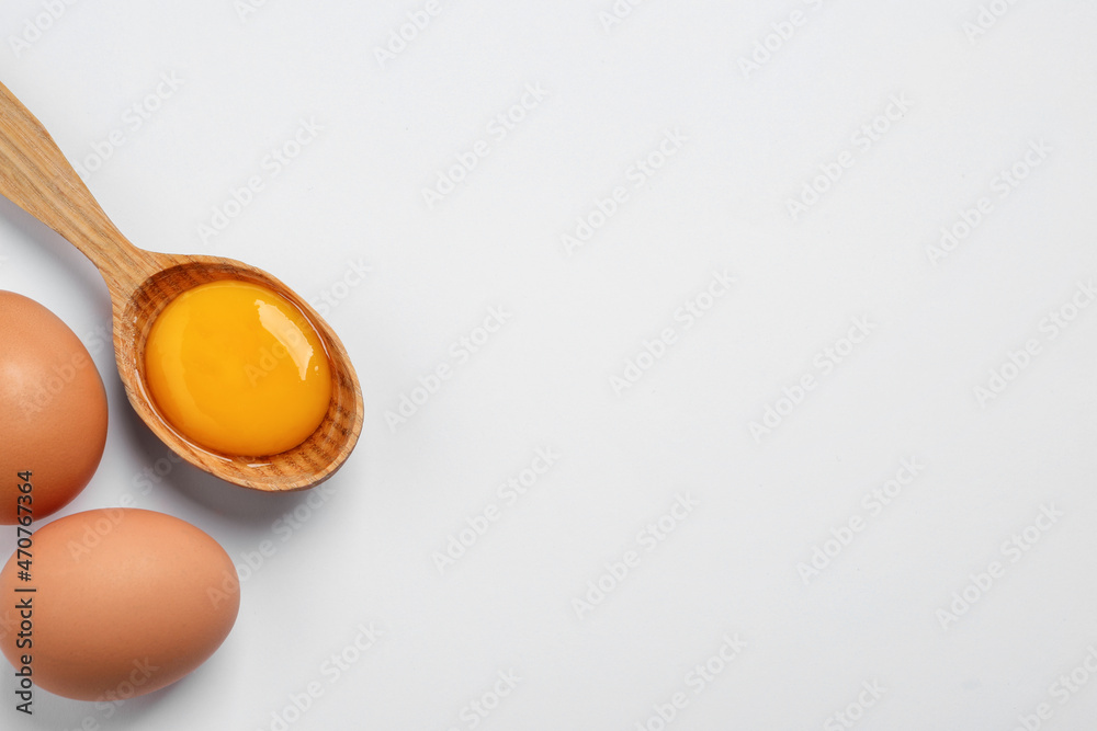 Obraz premium Raw chicken eggs and spoon with yolk on white background, flat lay. Space for text