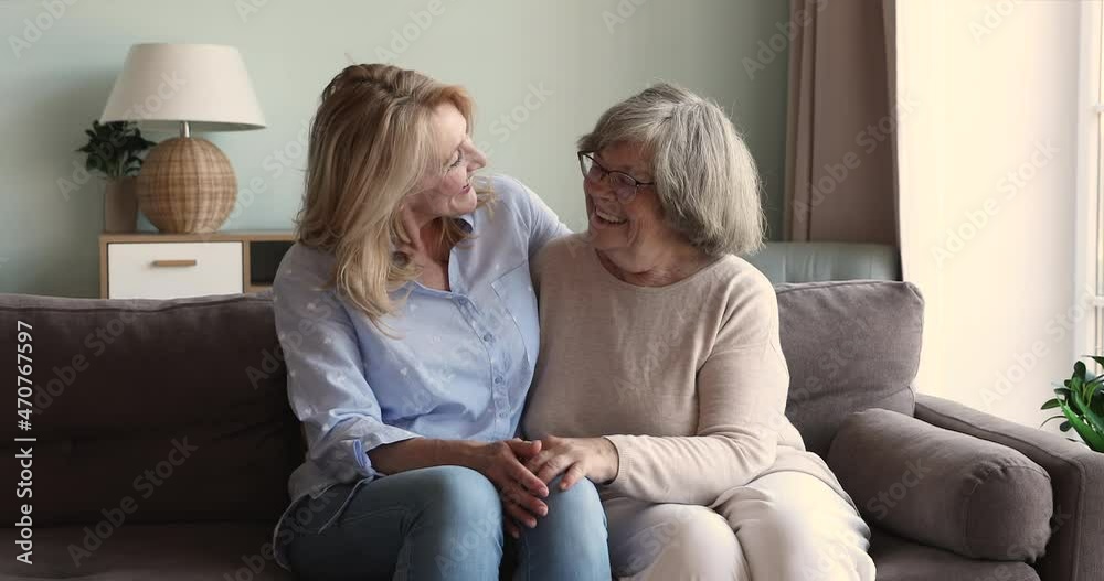 Loving mature daughter sit on couch close to elderly mother retiree hug her shoulders stroke silver hair with affection. Senior age mum having warm relationship with older adult female her beloved kid Loving mature daughter sit on couch close to elderly mother retiree hug her shoulders stroke silver hair with affection. Senior age mum having warm relationship with older adult female her beloved kid