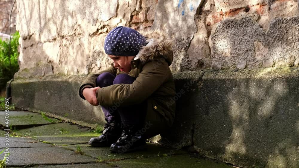 Sad Depressed Caucasian Girl Crying and Sitting Huddled Alone By the Wall Outdoors Holding Her Knees