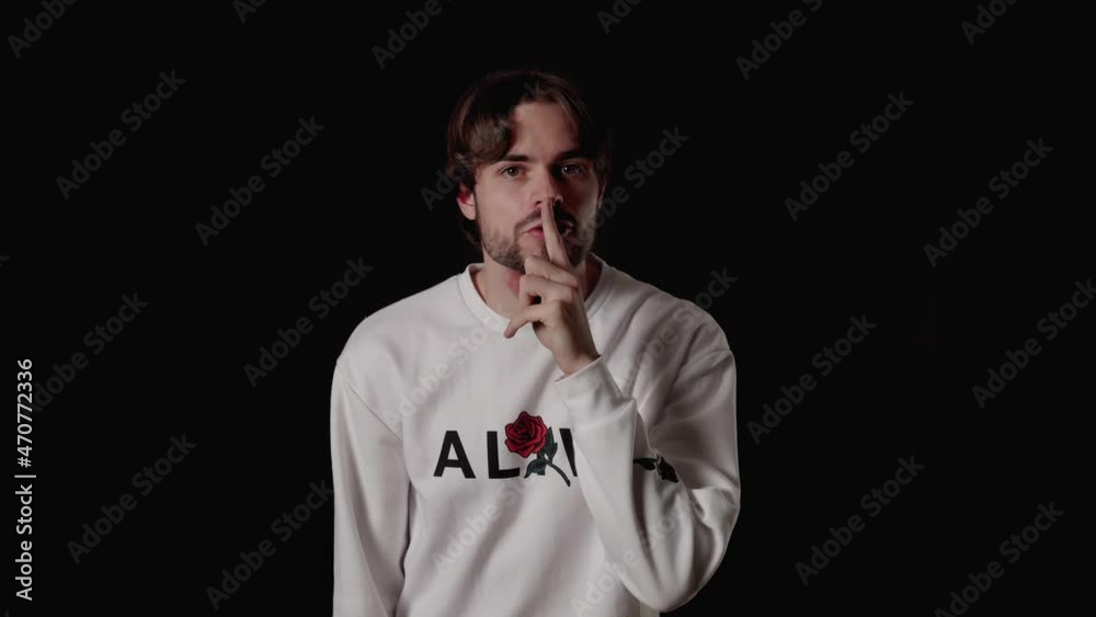 Trendy Young Man shushing into the camera, silence gesture, wide, black background Trendy Young Man shushing into the camera, silence gesture, wide, black background