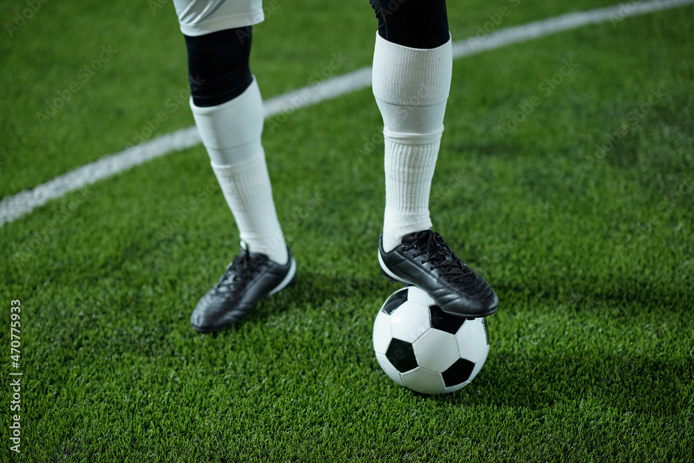 Fototapeta premium Legs of contemporary young footballer with his foot on soccer ball standing on the field and waiting for start of game