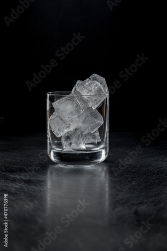 A rock glass with ice on a black background in the backlight.