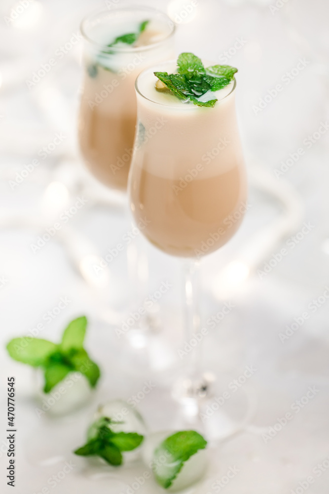 Glass of Irish cream liquor with ice and mint leaves closeup on light grey background
