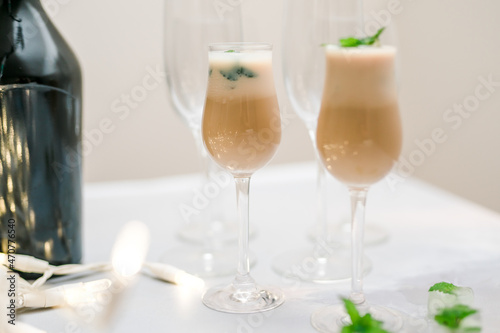 Irish cream liquor in glasses with frozen mint leaf ice cubes close up on light background
