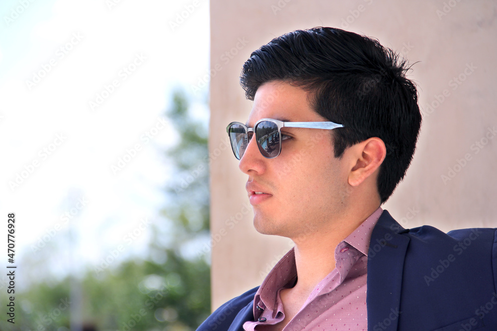 Close up of male model with sunglasses, in profile, wearing blue coat and pink shirt. Young business man with casual look. Close up of male model with sunglasses, in profile, wearing blue coat and pink shirt. Young business man with casual look.