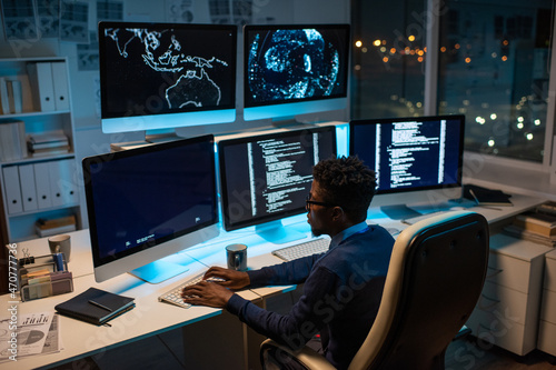 Young contemporary software developer working with decoded data while sitting in front of computer monitor in office at night