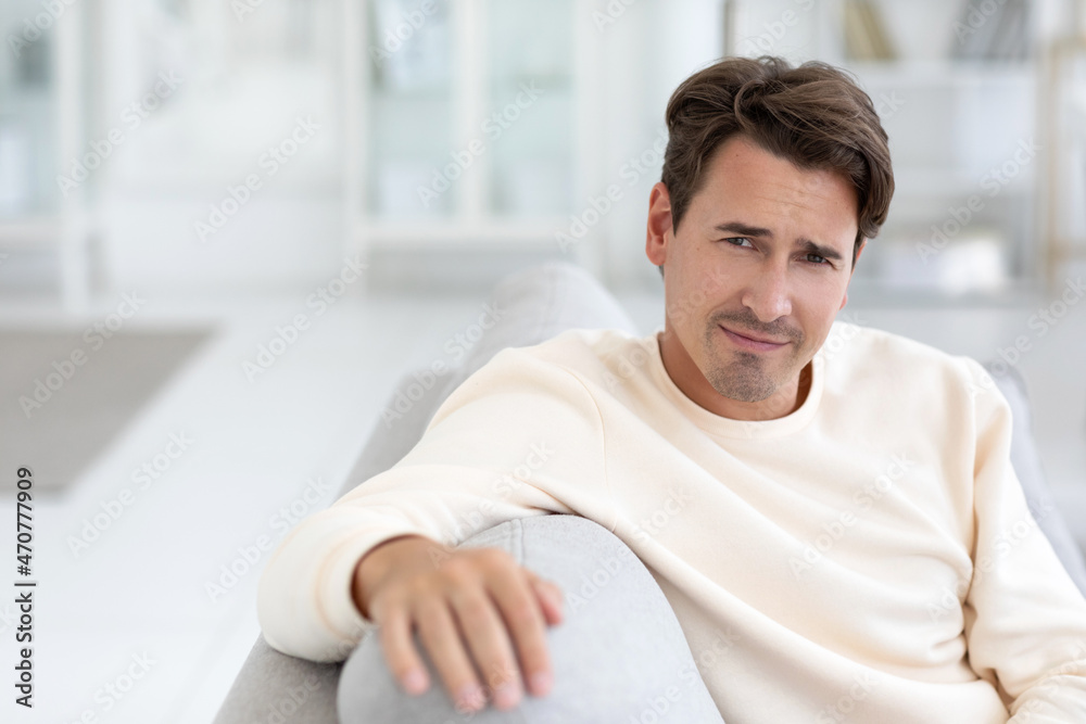 Close-up portrait of a handsome calm man has an attractive appearance, sits on a sofa against a cozy interior. Close-up portrait of a handsome calm man has an attractive appearance, sits on a sofa against a cozy interior.