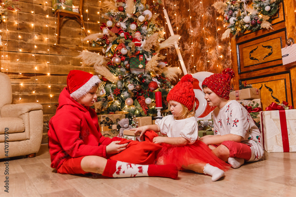children in red costumes sit under the tree and open Christmas gifts