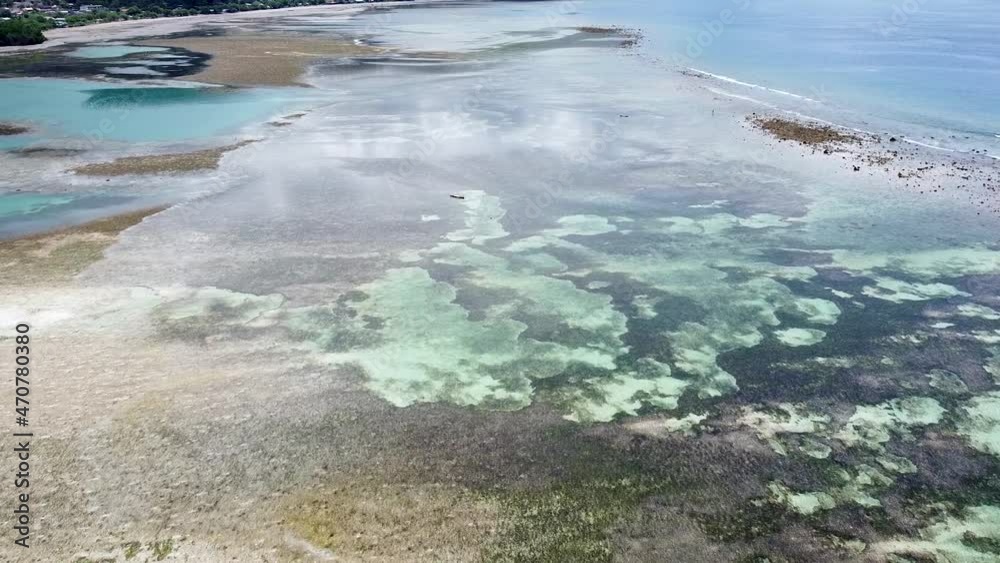 Aerial drone over a solo traditional fishing canoe boat at low tide with sand bars, coral reefs and crystal clear water on tropical island paradise Aerial drone over a solo traditional fishing canoe boat at low tide with sand bars, coral reefs and crystal clear water on tropical island paradise