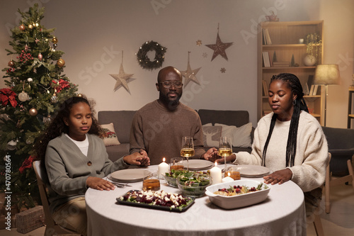 Contemporary Christian family of three praying before festive dinner while sitting by table served with homemade food