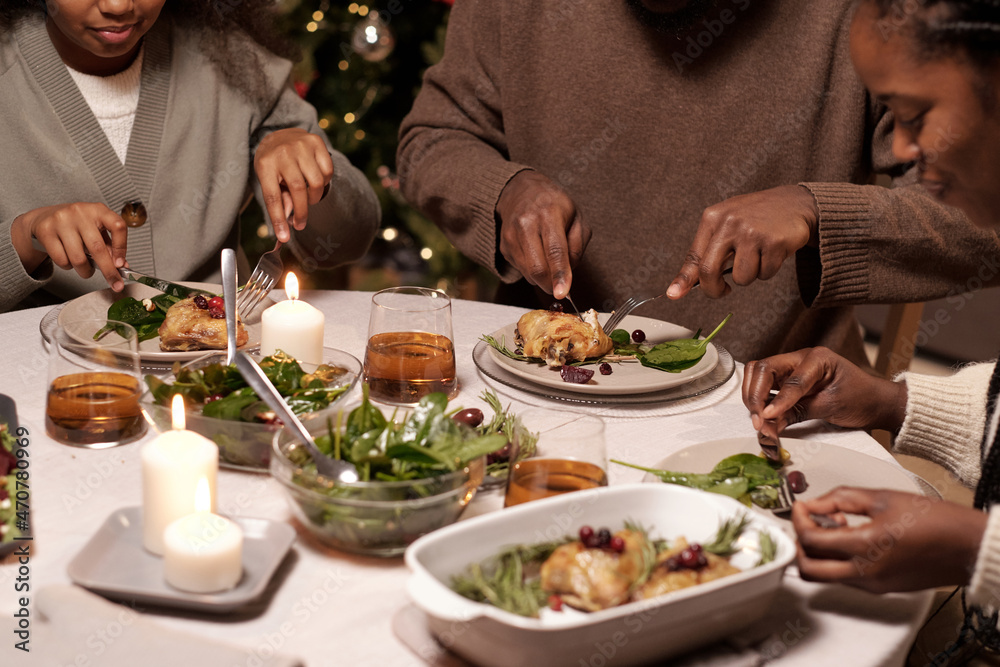 Hands of family members cutting appetizing meat on their plates while having festive dinner on Christmas day Hands of family members cutting appetizing meat on their plates while having festive dinner on Christmas day