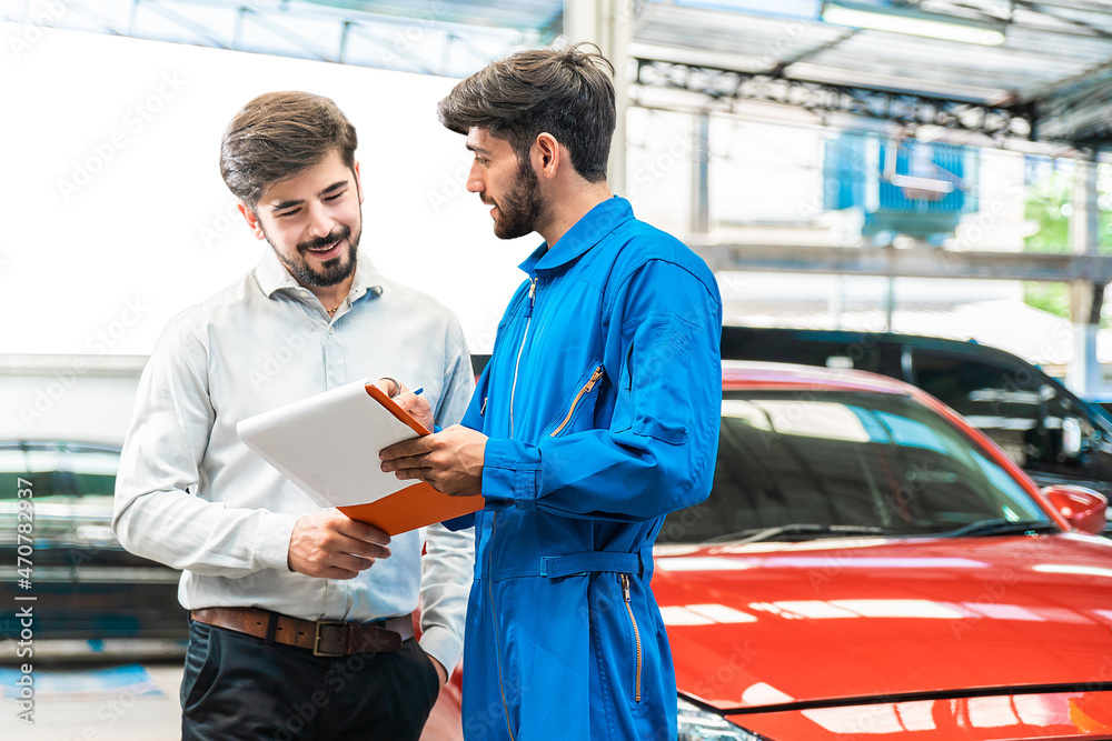Mechanic show the car checking list to customer before giving him a car key with the blur lifted car in the garage. Focus on customer. Auto car repair service center. Professional service. Mechanic show the car checking list to customer before giving him a car key with the blur lifted car in the garage. Focus on customer. Auto car repair service center. Professional service.