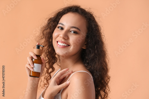 Beautiful African-American woman with cosmetic product in bottle on color background