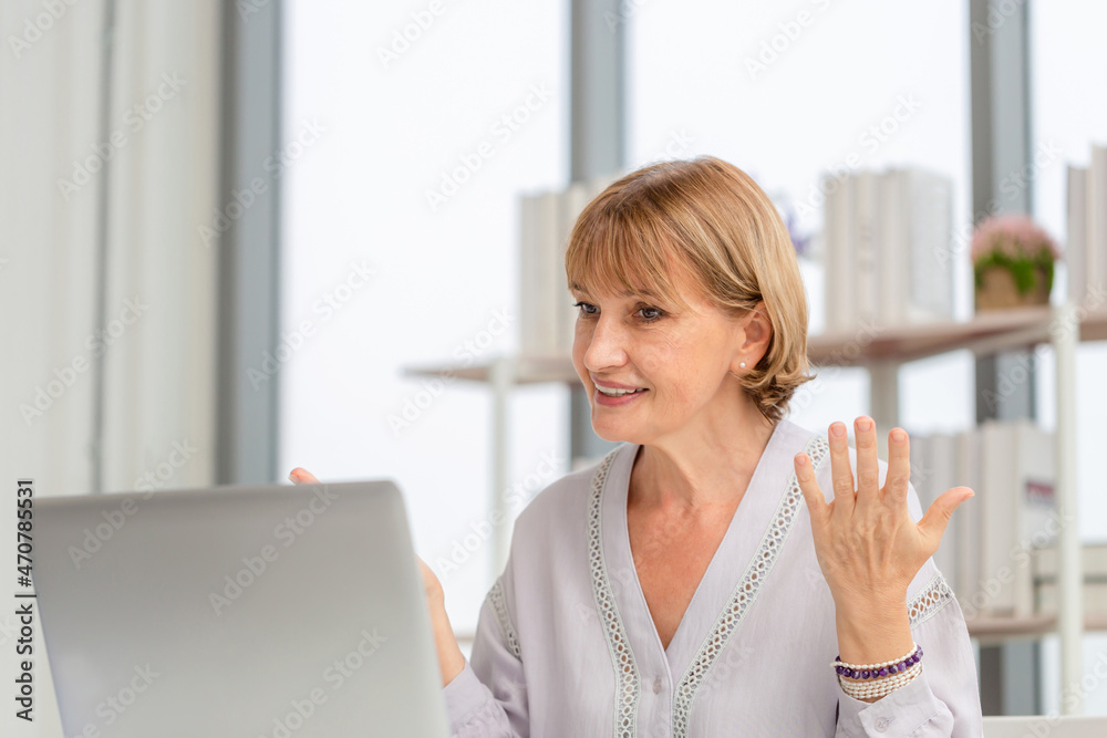 Portrait of woman using laptop and smartphone at home, Mature woman in living room with laptop talking video call on modern computer gadget