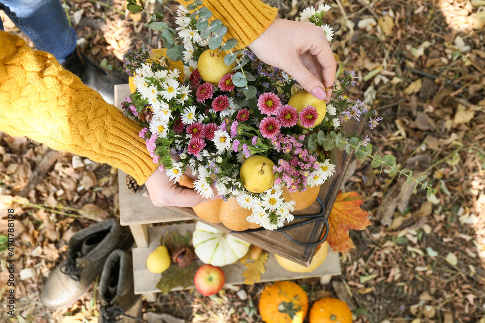 Woman making beautiful bouquet of autumn flowers in pumpkin outdoors - obrazy, fototapety, plakaty 