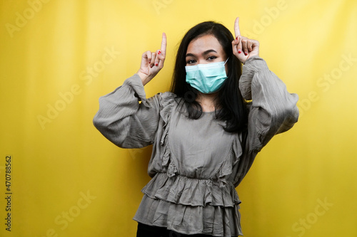 Beautiful young woman wearing a mask with hands pointing up, presenting something, isolated