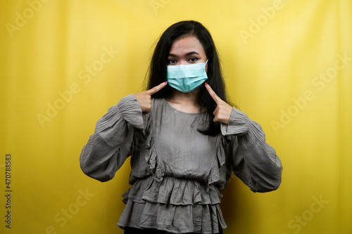 Beautiful young woman wearing a mask with hand pointing at the mask, isolated