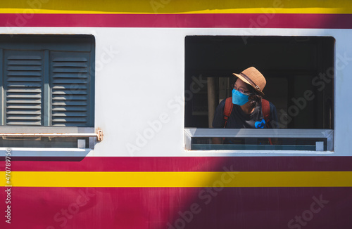 Asian female traveler wears protective mask leaning out and looking sideway from window of the old train at railway station photo