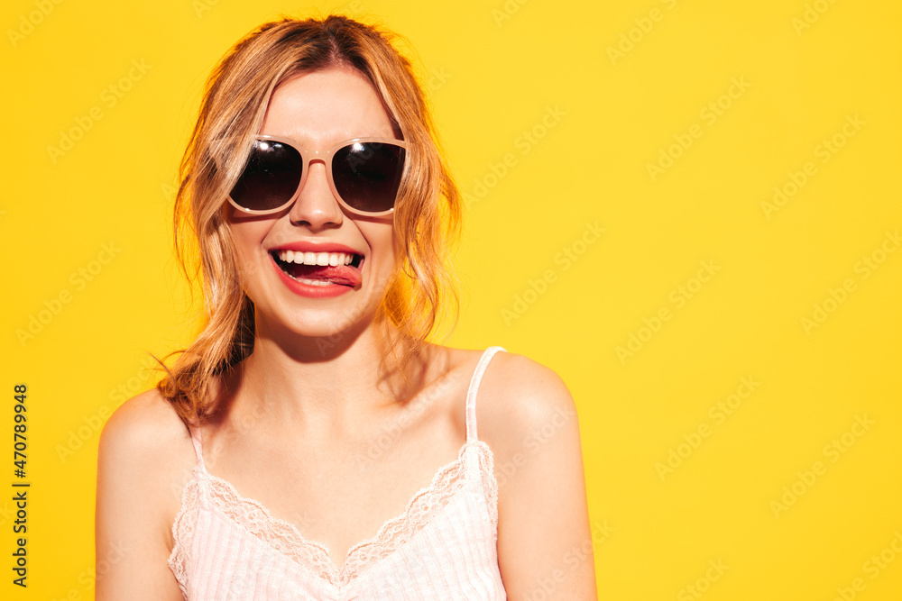 Young beautiful smiling female in trendy summer clothes. Sexy carefree woman posing near blue yellow in studio. Positive model having fun. Cheerful and happy. In sunglasses. Shows tongue Young beautiful smiling female in trendy summer clothes. Sexy carefree woman posing near blue yellow in studio. Positive model having fun. Cheerful and happy. In sunglasses. Shows tongue