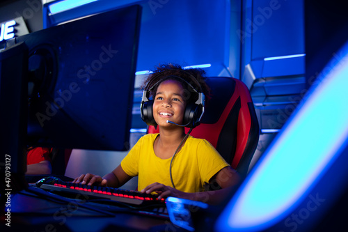 Portrait of excited African American girl with headset playing video games on computer in game room.