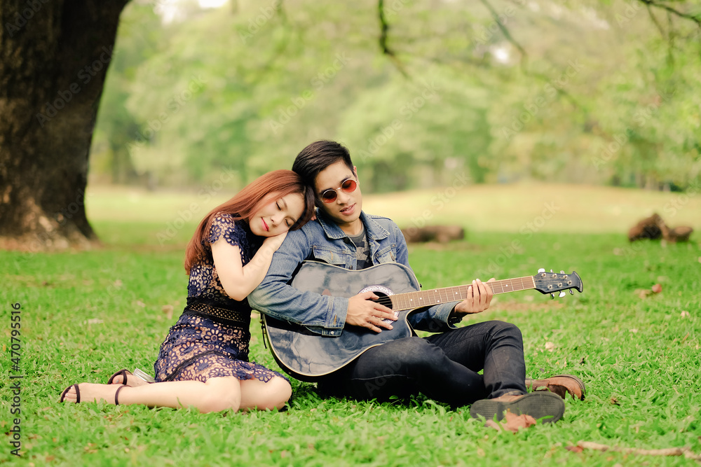 Portrait asia young couple in love, boyfriend and girlfriend playing guitar in park happy summer life
