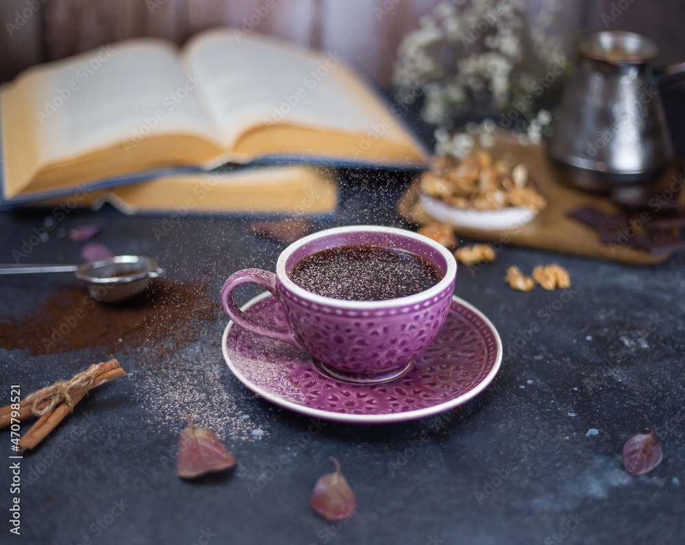 sprinkle cinnamon powder on hot coffee on a dark wooden background with open books