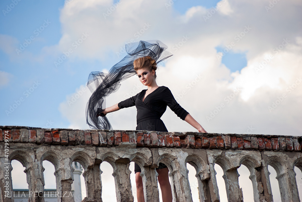 Young woman with elegant dress with castle and cloudy sky on the background with flying fabric on a classic terrace Young woman with elegant dress with castle and cloudy sky on the background with flying fabric on a classic terrace