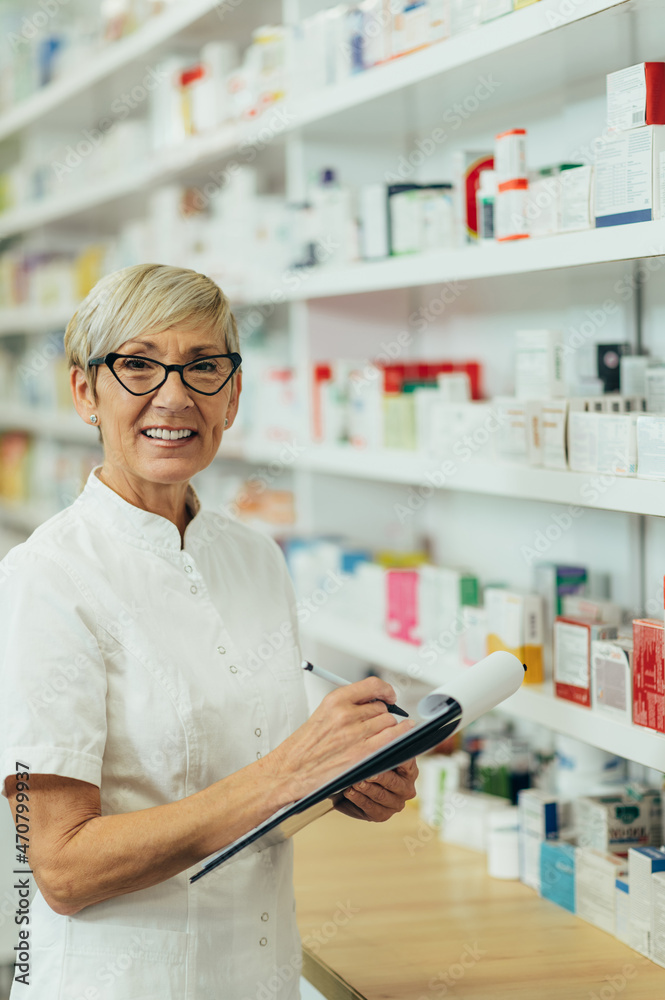 Obraz premium Beautiful senior female pharmacist checking medications on a shelf