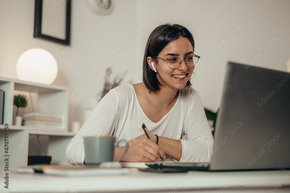 Woman writing in a notebook and using a laptop while working from home Woman writing in a notebook and using a laptop while working from home