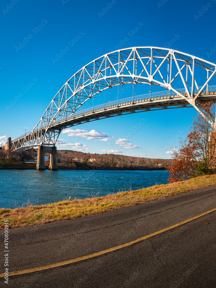 Obraz premium Sagamore Bridge and paved bikeways along the Cape Cod Canal. Peaceful and safe outdoor recreational park in Bourne, Massachusetts. Arching landmark metal bridge connecting Massachusetts mainland to Ca