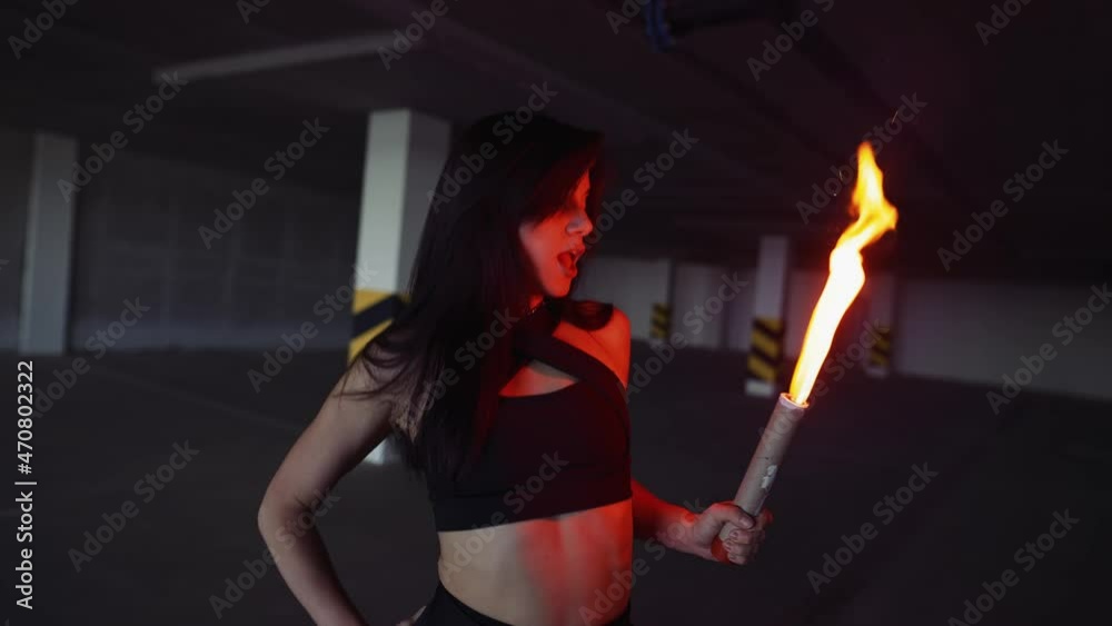 Sensual woman performs modern dance, posing to the camera in parking zone in dark light with fire torch