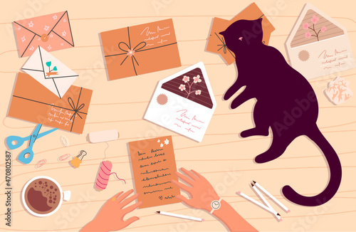 Funny cat lying and watching the woman's hands on the table. Top view of the desk with a sheet of paper, letters, cat, scissors, coffee, notepad, crumpled paper balls and supplies.