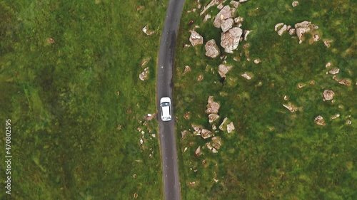 Aerial top view of generic electric car driving on country road in Faroe islands.Wild nature, green meadow, rocks. Ecology friendly auto riding on electric charge along motorway photo