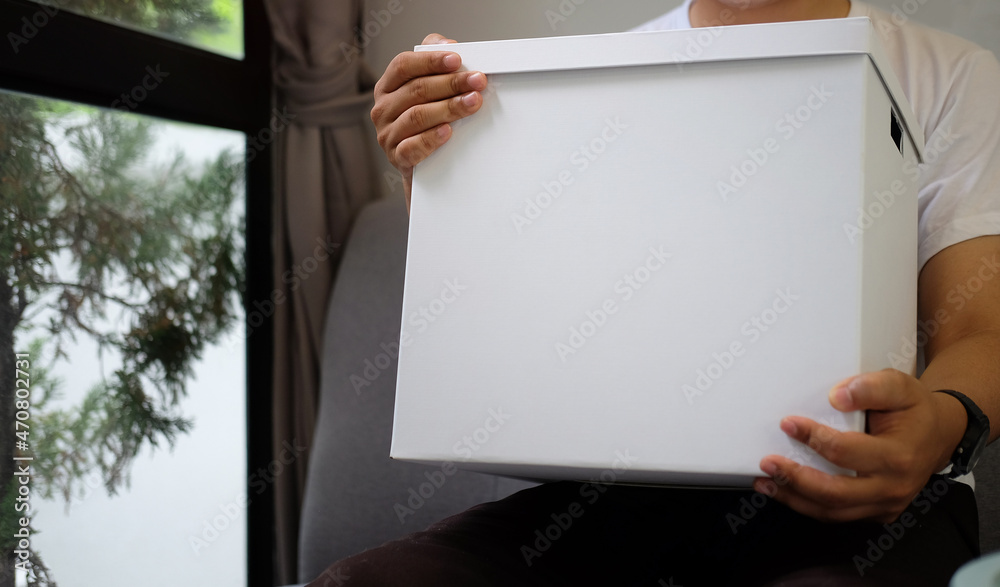 Cropped shot young man holding cardboard box with parcel while sitting on sofa at home. Cropped shot young man holding cardboard box with parcel while sitting on sofa at home.