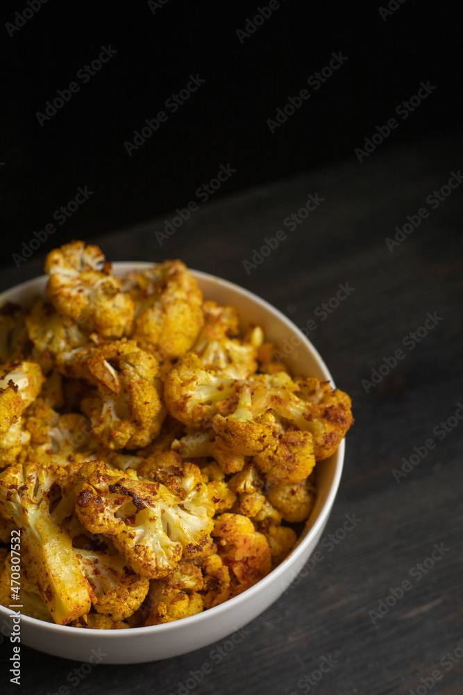 Baked cauliflower in white bowl on dark wooden desk, black background. Top view. Baked cauliflower in white bowl on dark wooden desk, black background. Top view.