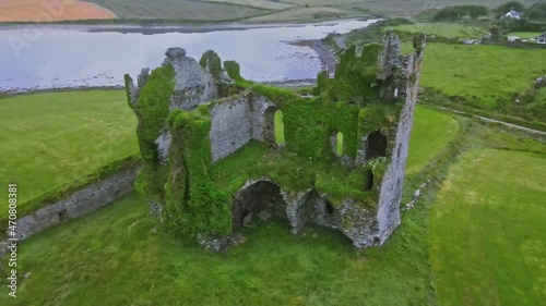 Drone video of the Ballycarbery castle, ingrown ruin in Ireland with fields and sea at the background.