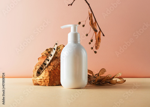 White plastic bottle with pump and brick and natural plant parts creative still life cosmetic photography. Lotion, shampoo, soap, hair conditioner blank empty mockup. Trendy composition