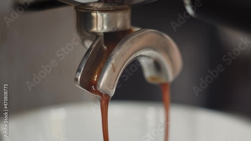 Freshly brewed coffee flowing out of a coffee machine and into a cup. The liquid is dark brown at first, then becomes lighter and creamier until it is very watery. Shallow depth of field. photo