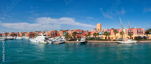 Scenic panoramic view from the marina of Hurghada to moored sailing yachts, boats, ships and the city's promenade with shops, cafes and a pedestrian zone for walking in the background