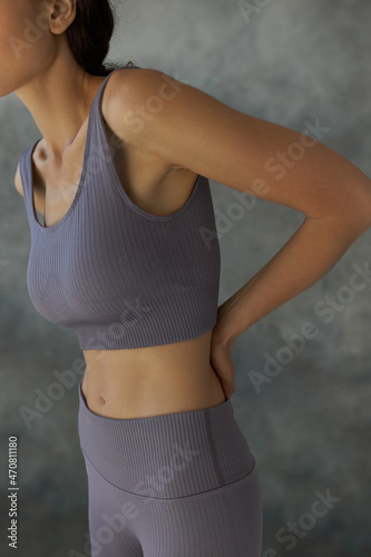 Crop shot of perfect female body in fitness clothes getting ready to start training workout or participate in sports competition indoor, standing against grey studio wall, stroking loin