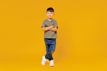 Full body little small smiling happy boy 6-7 years old wearing green t-shirt hod hands crossed folded look camera isolated on plain yellow background studio Mother's Day love family lifestyle concept.